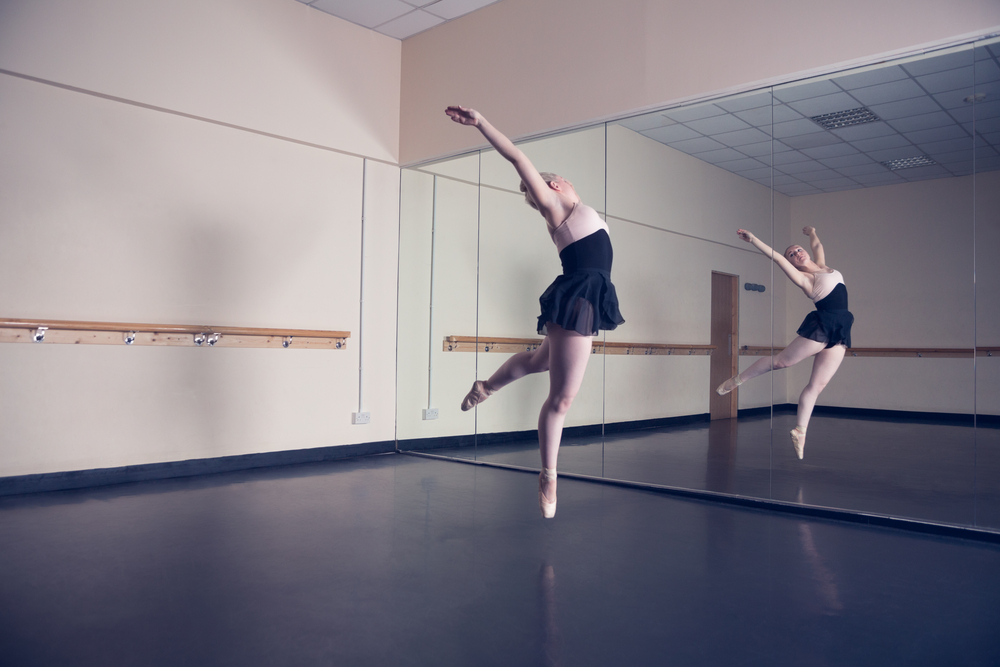 a ballet dancer infront of a mirror dancing in a commercial space