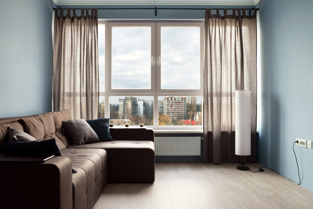 a small room with a brown couch and a large window looking out to a city landscape